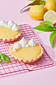 Tasty lemon tarts with whipped cream served on pink background with fresh citruses