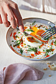Crop anonymous person eating Turkish egg using fork and knife near napkin