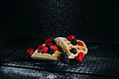 Sweet waffles served with fresh berries and sugar powder on black background