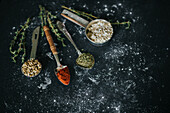 Spoons with paprika and dry herbs placed on black table with oat and sunflower seeds