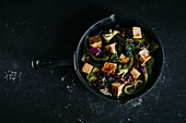 Vegetarian salad with fried tofu and vegetables served on black background