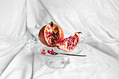 Fresh pomegranate with ripe seeds and blooming flower sprig on transparent stand on crumpled fabric