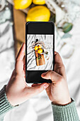 Zitronen in Einkaufsnetz auf Holzbrett mit Smartphone fotografieren