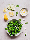 Spinach and mint leaves in bowl for salad against cucumber slices and sauce with lemon zest