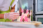 Konditorin mit Handschuh verziert Kuchen mit bunter Schokolade