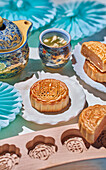 Traditioneller Mondkuchen mit Füllung, Backform, Teekanne und Teebecher mit Kräutertee