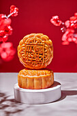 Round Chinese traditional sweets baked mooncakes served on stand on table with flowers against red background