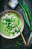 Bowl with creamy pea soup served on table with black napkins and green onion