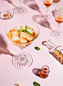 Glass with whiskey and ice cubes garnished with basil leaves served on pink table with shiny goblets