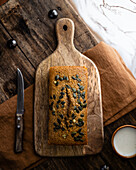 Wholegrain freshly baked loaf placed on wooden cutting board near knife and cup of milk