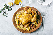 Roasted chicken garnished with slices of roasted potatoes and seasoned with fresh rosemary