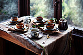 Set wooden table with ceramic cups and teapot by the window