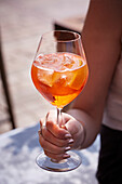 Hand holding stemmed glass with Aperol Spritz