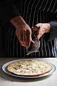 A waiter Shaving truffles onto a pizza base