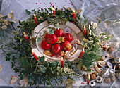 Red apples with biscuits in a bowl surrounded by ivy wreath with candles (Christmas)
