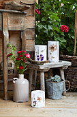 Gartendeko aus Windlichtern mit Trockenblumen, Vase mit Blumen, Holzhocker und Sukkulente