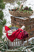 Korb mit Decken, Thermosflasche und Plätzchen im Garten, Weihnachtsdekoration auf Ziegelmauer