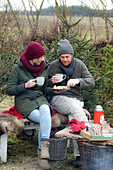 Man and woman with mulled wine and Christmas biscuits sitting on bench in garden