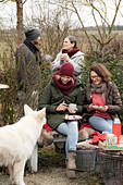 Freunde mit Glühwein und Weihnachtsgebäck im Garten, im Vordergrund Hund