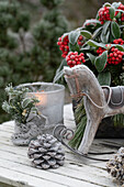 Weihnachtsdekoration mit Skimmie (Skimmia), Windlicht, kleinem Schaukelpferd und Zapfen