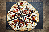 A pizza topped with halloumi, black olives and peppers, sliced on a slate platter