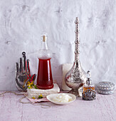 A glass flacon of St. John's wort oil with a bowl of coconut oil in front of it and oriental flacons with a metal look next to it (variety of oils)