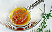Glass bowl with red wine vinegar olive oil vinaigrette and a whisk