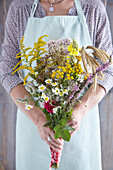 A woman in an apron holding a bouquet of herbs