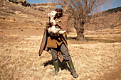 Einheimischer Hirte des Basotho-Volkes mit einem Lamm im Hochland, Königreich Lesotho, Südafrika