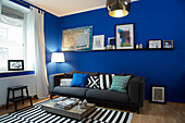 Polstersofa und schwarz-weiß gestreifter Teppich im Wohnzimmer mit blauen Wänden