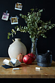 Table with mortar, pomegranates, vase and eucalyptus branches in front of black wall