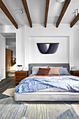 Doppelbett, darüber Wandbehang in weißem Schlafzimmer mit Holzbalken
