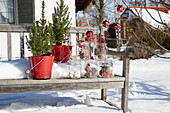 Holzbank im Schnee mit Mini-Tannenbäumen, Zapfen in Gläsern und Weihnachtskugeln