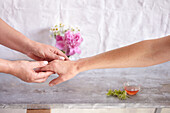Zwei Hände ergreifen eine Hand für eine Handmassage (Zuwendung), Schälchen mit Aromaöl
