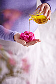 Woman pouring aromatic oil from a perfume bottle into a peony blossom