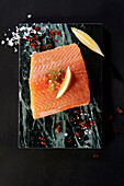 Salmon with lemon, chili and salt on marble plate and black background