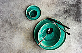 Green earthenware dishes with cutlery on a concrete surface