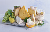 Various cheeses with grapes and pear on a light background