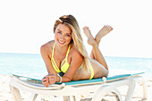 Young blonde woman in a yellow bikini lying on a lounger by the sea