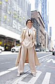 A brunette woman wearing a beige trouser suit and a long coat walking down the street