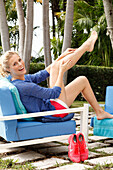 Blonde Frau sitzt auf einem Outdoor-Sessel und massiert sich die Beine