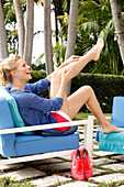 Blonde Frau sitzt auf einem Outdoor-Sessel und massiert sich die Beine