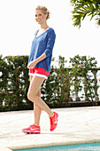 A blonde woman wearing a blue shirt, red shorts and sports shoes