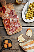A selection of cured meats on a wooden board with bread and olives on the side