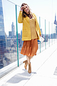 Long haired woman in orange skirt, yellow knit sweater and short coat