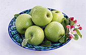 Schale mit grünen Äpfeln und Apfelblüte
