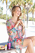 Young blond woman in a colorful beach dress sitting on a bench