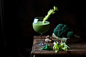 Grüner Gemüse-Smoothie auf Holztisch vor schwarzem Hintergrund