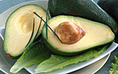 Whole and two halved avocados on lettuce leaves
