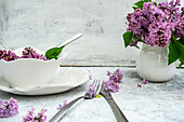 Frühlingsgedeck mit Fliedern auf Tisch im Freien
